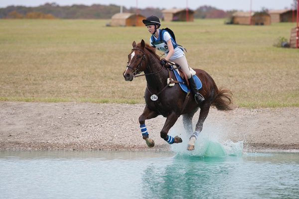 Getting started in eventing. A young girl gallops her horse through the water on a cross-country course