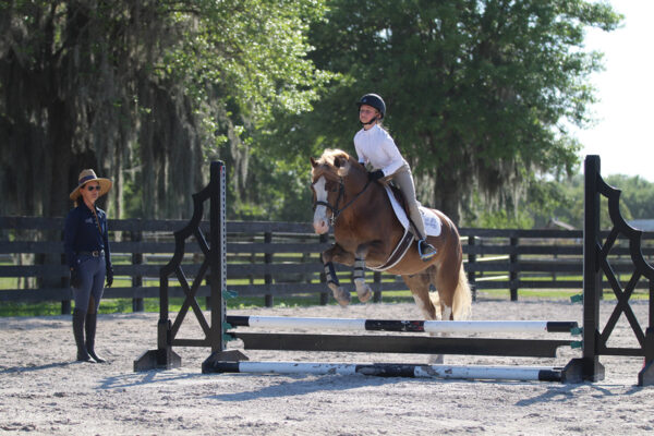 A young rider jumping her pony with a trainer's instruction