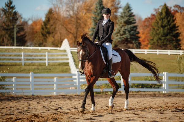 A rider competing in dressage with fall foliage in the background