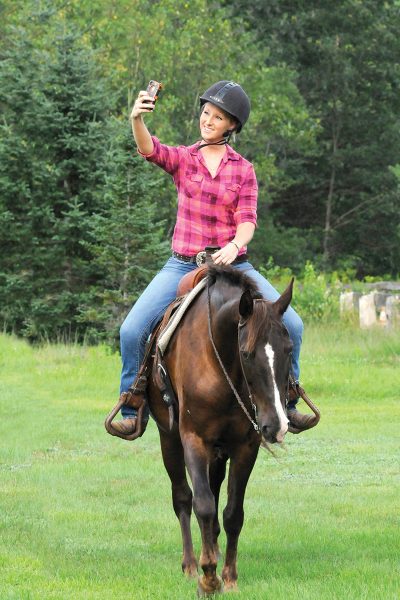 A girl takes a cell phone picture while trail riding