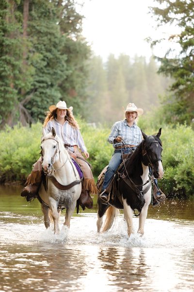 Showing an image of Two trail guides riding horses in a river.