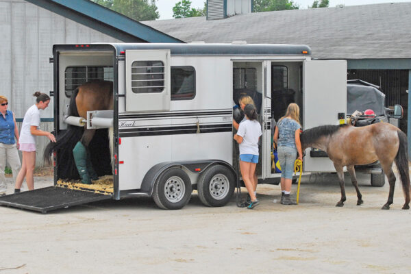 Young riders practice safety protocols while loading horses in a trailer