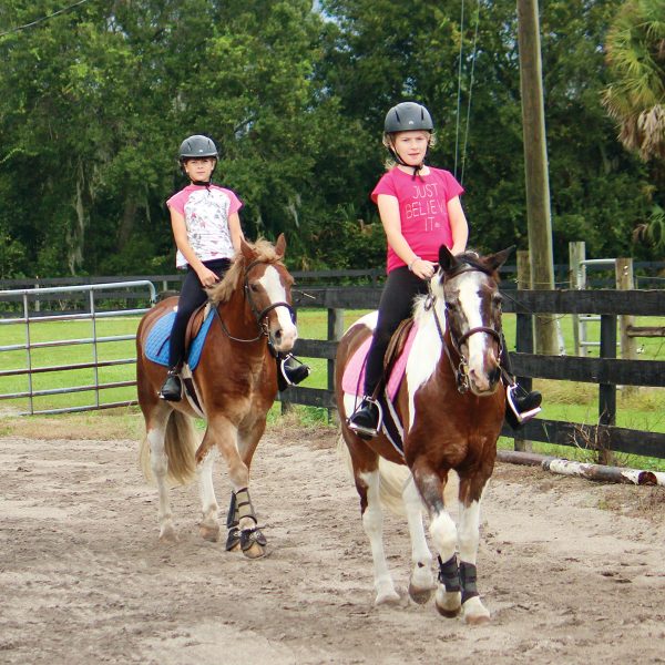 Two young riders riding lesson horses.