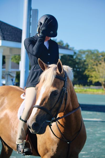A young rider touches her riding helmet while on her palomino horse.