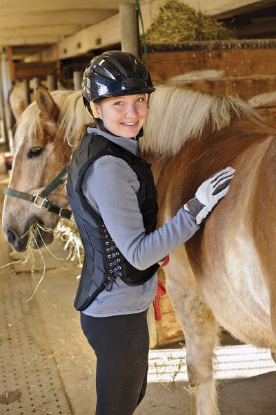 A young rider with her pony, wearing a riding safety vest