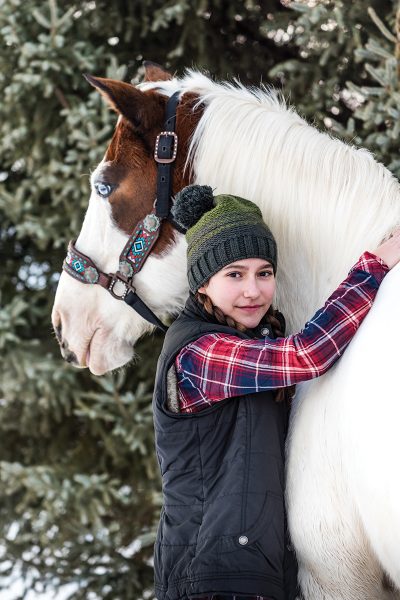 A young girl with a blue-eyed pinto gelding in the snow.