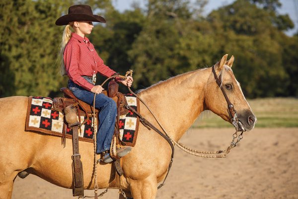 A young rider sits on a palomino horse in western tack