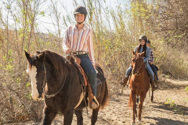 A group of girls are shown riding their horses with ASTM-approved helmets and going with buddies, which are among the top trail riding tips