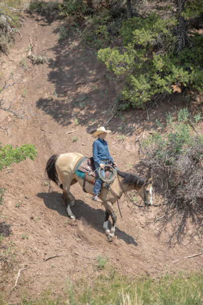 A young cowboy riding his horse down a hill