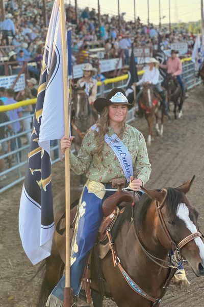 A smiling rodeo queen carrying a flag in the opening ceremonies