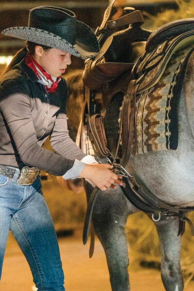 A young rider tightens her pony's cinch