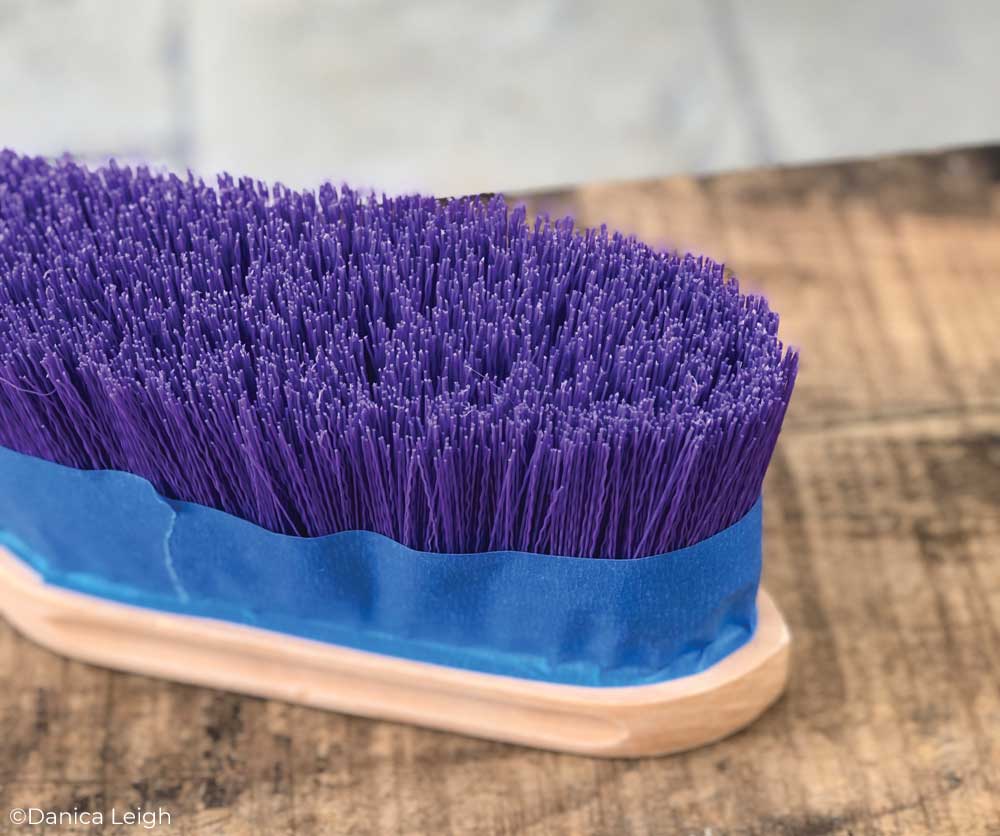 A horse brush with blue painters tape around the bristles.