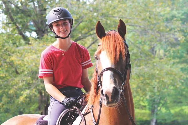 A young equestrian riding a chestnut with a blaze.