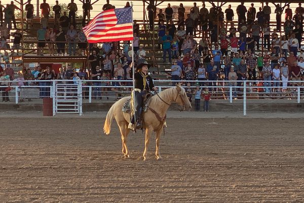 A cowgirl holds the American flag in the arena aboard a palomino for the national anthem