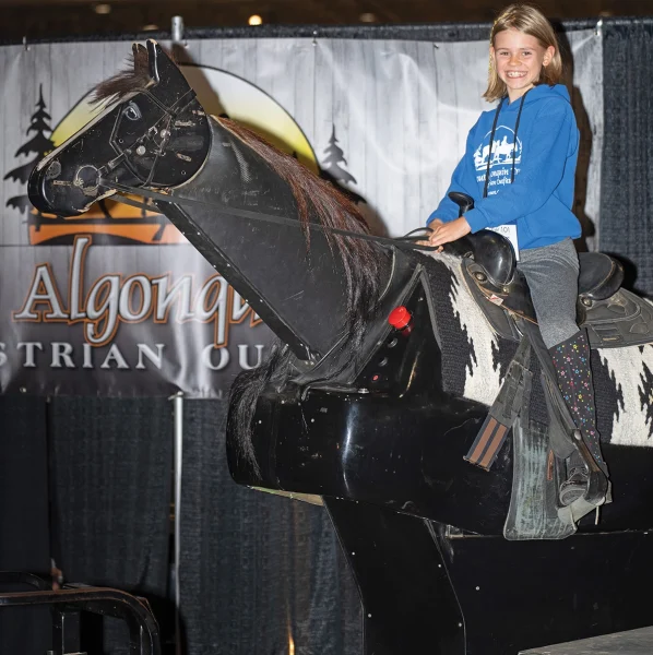 Serena, the youngest sister, sits on a horse simulator at Algonquin Trails’ booth at the Royal Winter Fair.