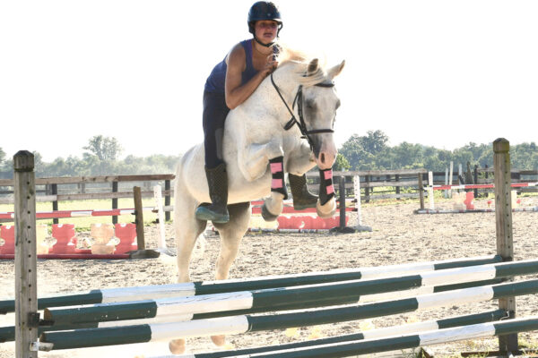 An equestrian jumping a pony